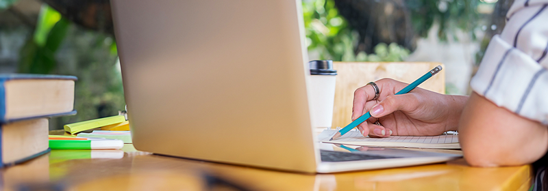 Closeup of a laptop with someone working on a paper